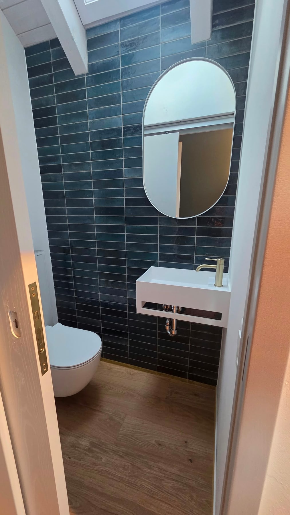 Gäste-WC mit blauen Wandfliesen, ovalem Spiegel und weissem Waschbecken